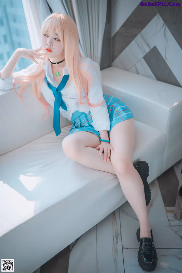 A woman sitting on a white couch with pink hair.