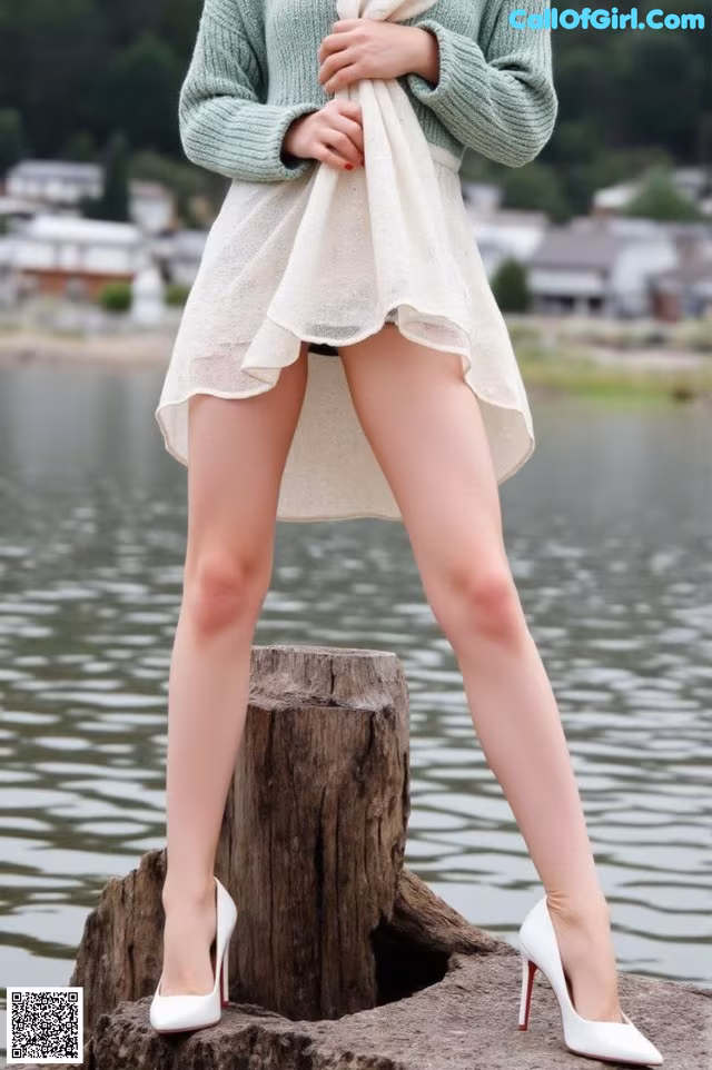 A woman standing on top of a tree stump by the water.