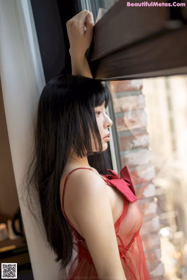 A woman in a red dress looking out a window.