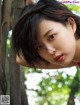 A woman leaning against a tree in a forest.