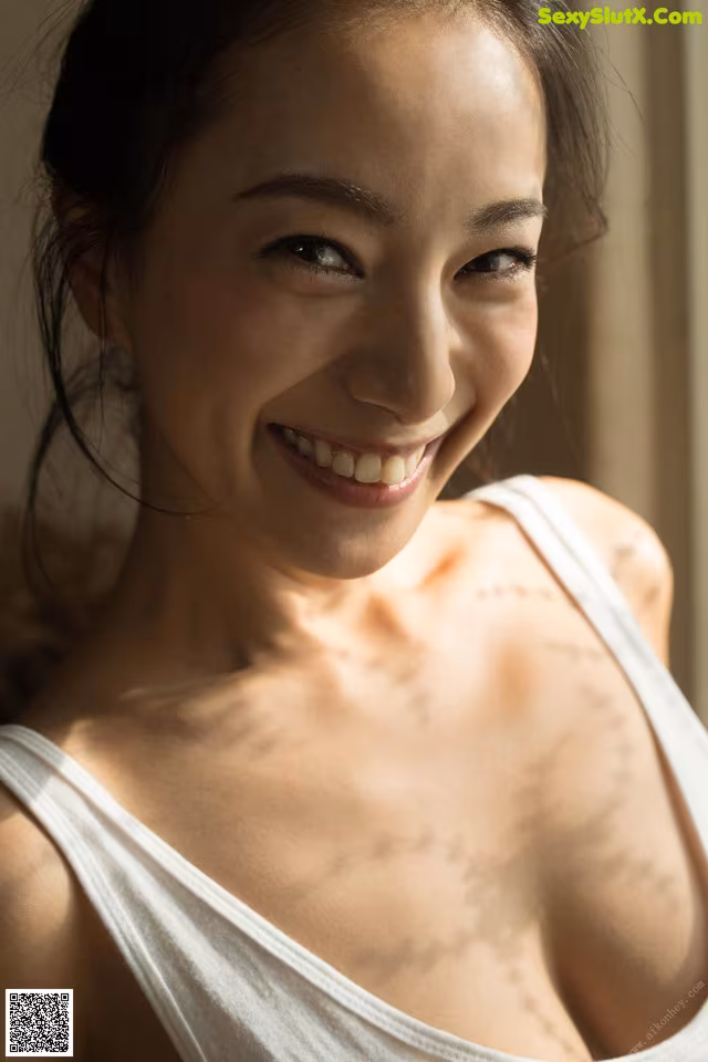 A woman in a white tank top smiles at the camera.