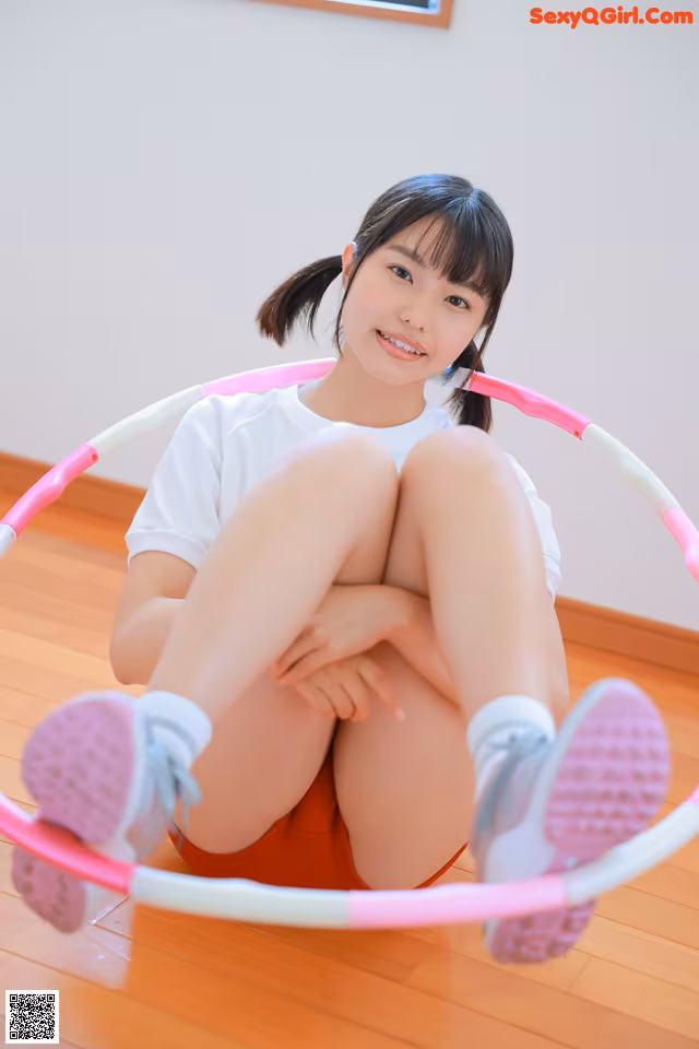 A young woman sitting on the floor with a hula hoop.