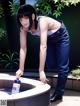 A woman in jeans and a tank top is pouring water into a fountain.