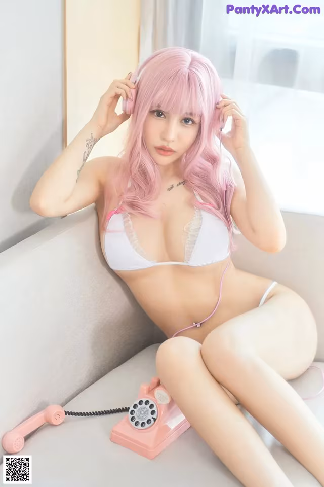 A woman with pink hair sitting on a couch talking on a phone.