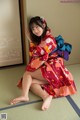 A woman in a red kimono sitting on a tatami mat.