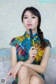 A woman in a cheongsam sitting on a couch holding a fan.