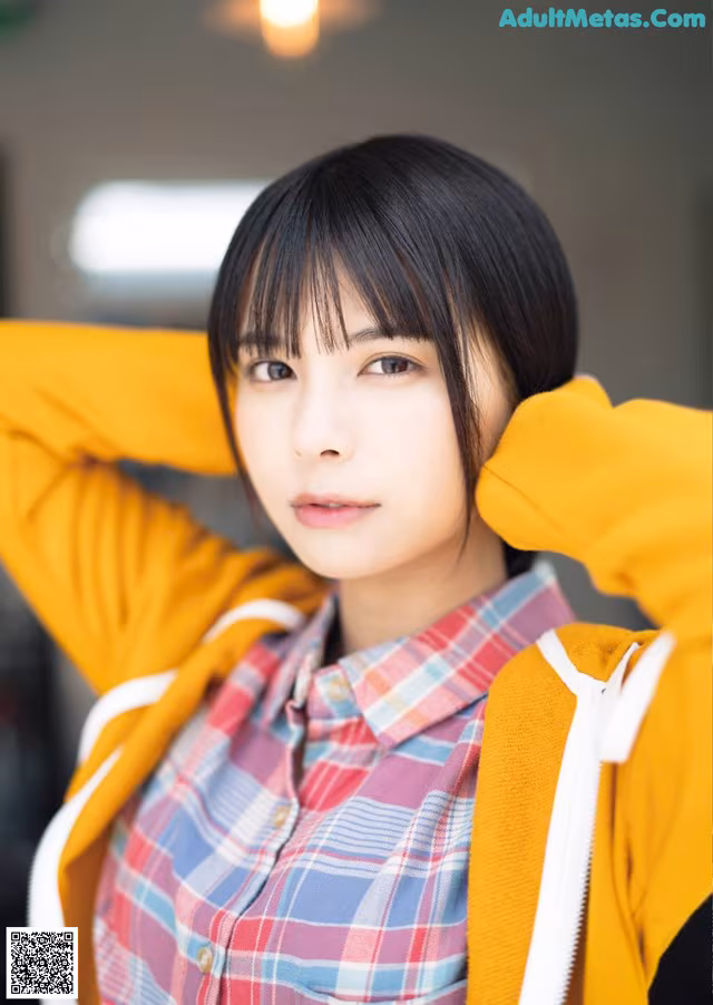 A young woman wearing a yellow jacket and a plaid shirt.