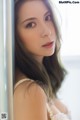 A woman with long brown hair leaning against a wall.