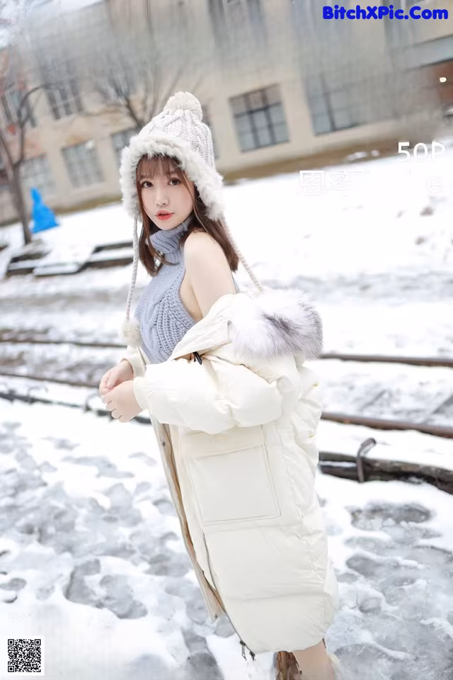 a woman in a white coat and hat standing in the snow