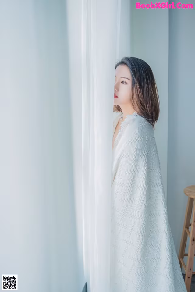 A woman in a white dress standing by a window.