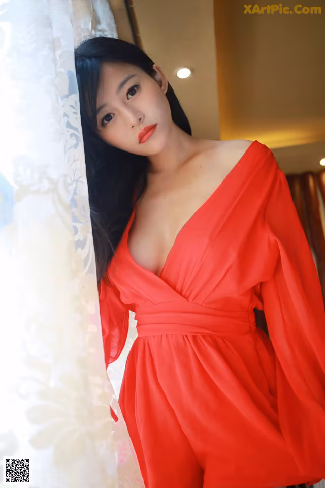 A woman in a red dress leaning against a curtain.