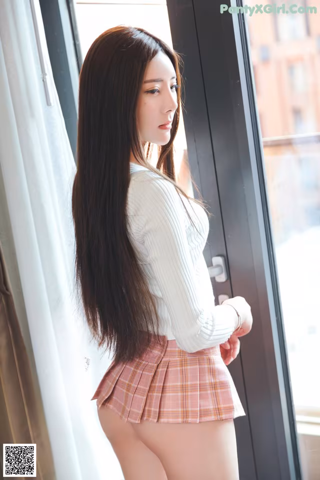 A woman with long black hair standing by a window.
