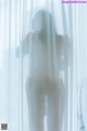 A nude woman standing in front of a white curtain.