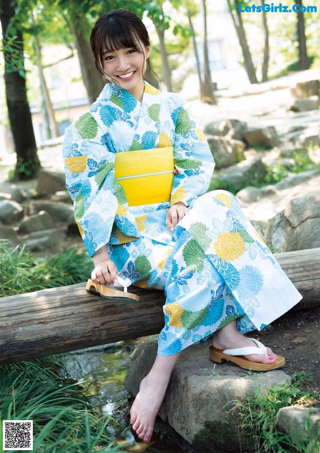 A woman in a blue and yellow kimono sitting on a log.