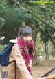 A woman wearing a scarf standing next to a wooden bench.