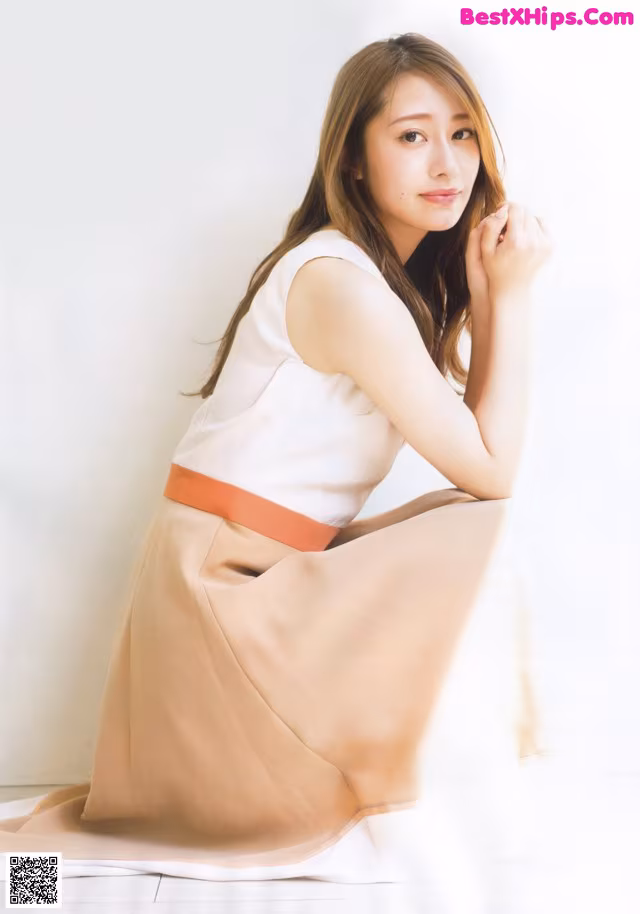 A woman in a white top and tan skirt posing for a picture.